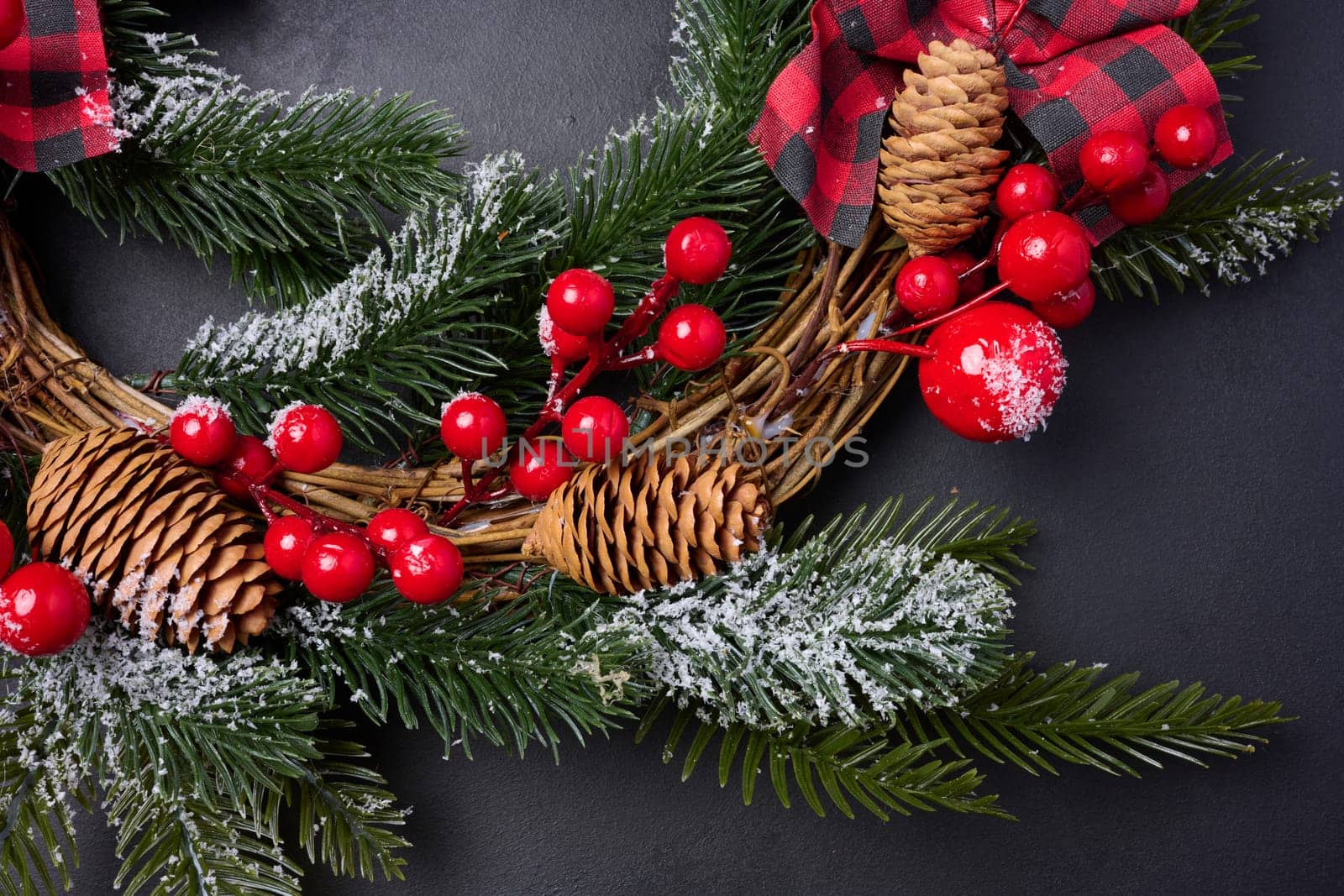 A circular Christmas wreath made of fir branches and other decorations on a black chalkboard