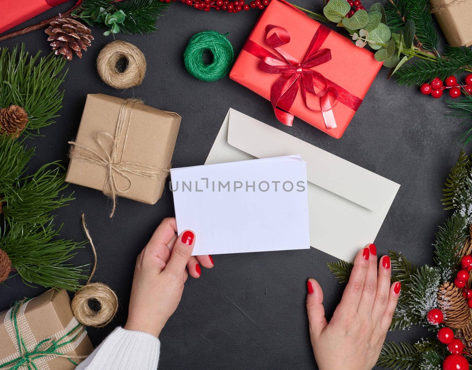 White envelope and Christmas wreath on a black background, top view. Woman sending a letter