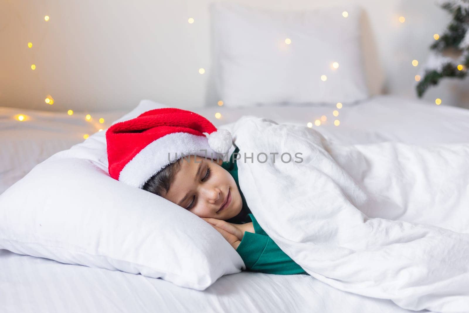 Sweet child boy sleeping in bed wearing Santa Claus hat in Christmas eve.