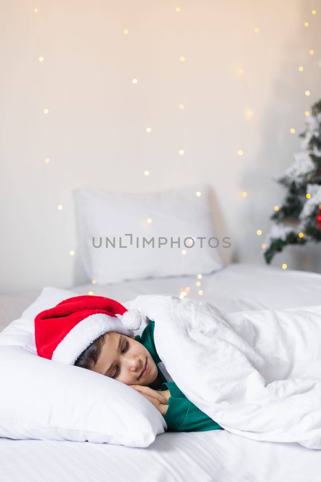 Sweet child boy sleeping in bed wearing Santa Claus hat in Christmas eve.