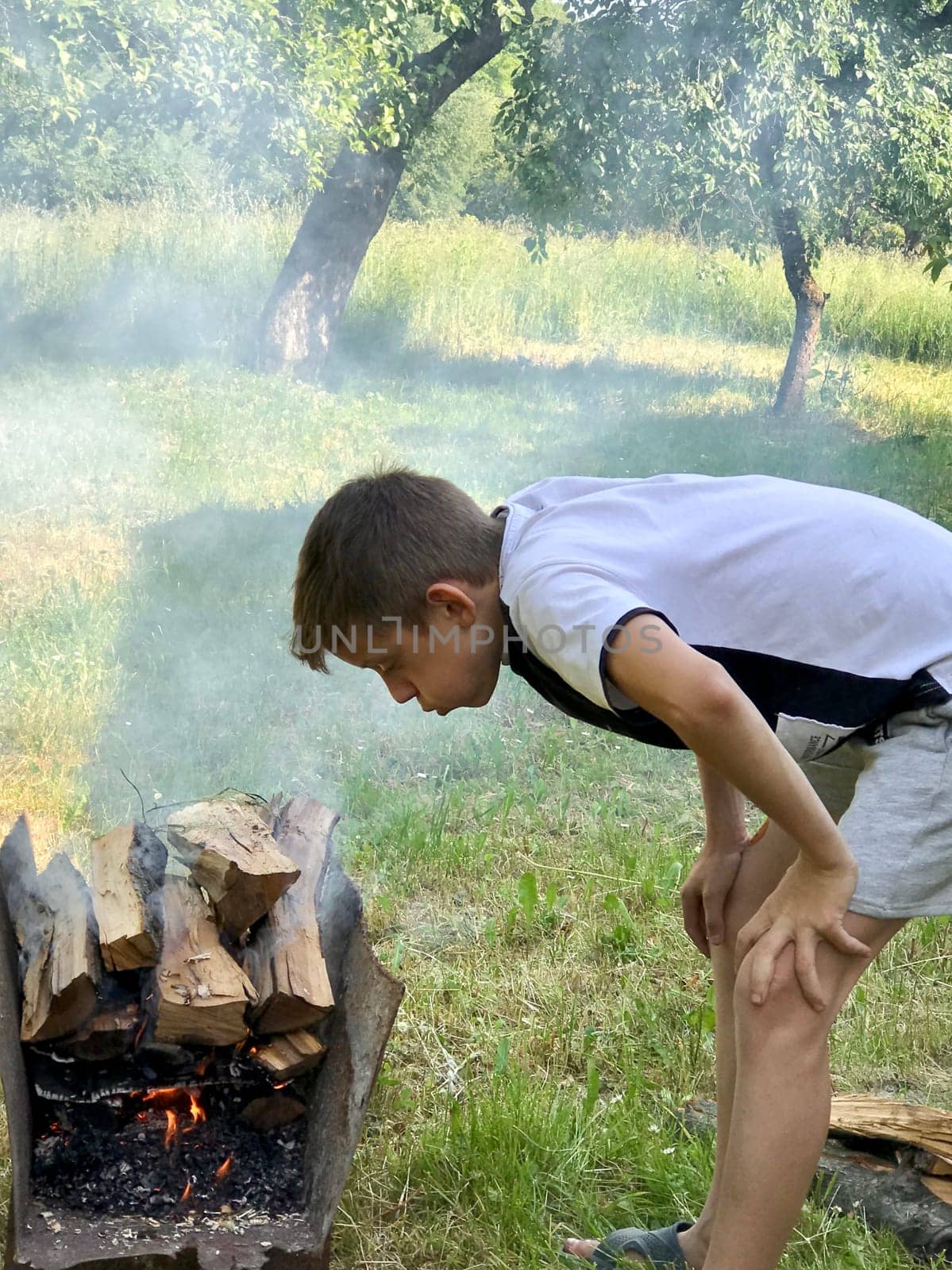 a twelve-year-old boy puts firewood in a barbecue grill in the garden