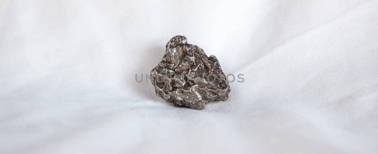 Nickel-iron type meteorite fragment. Isolated over white background. Placed over cotton cloth