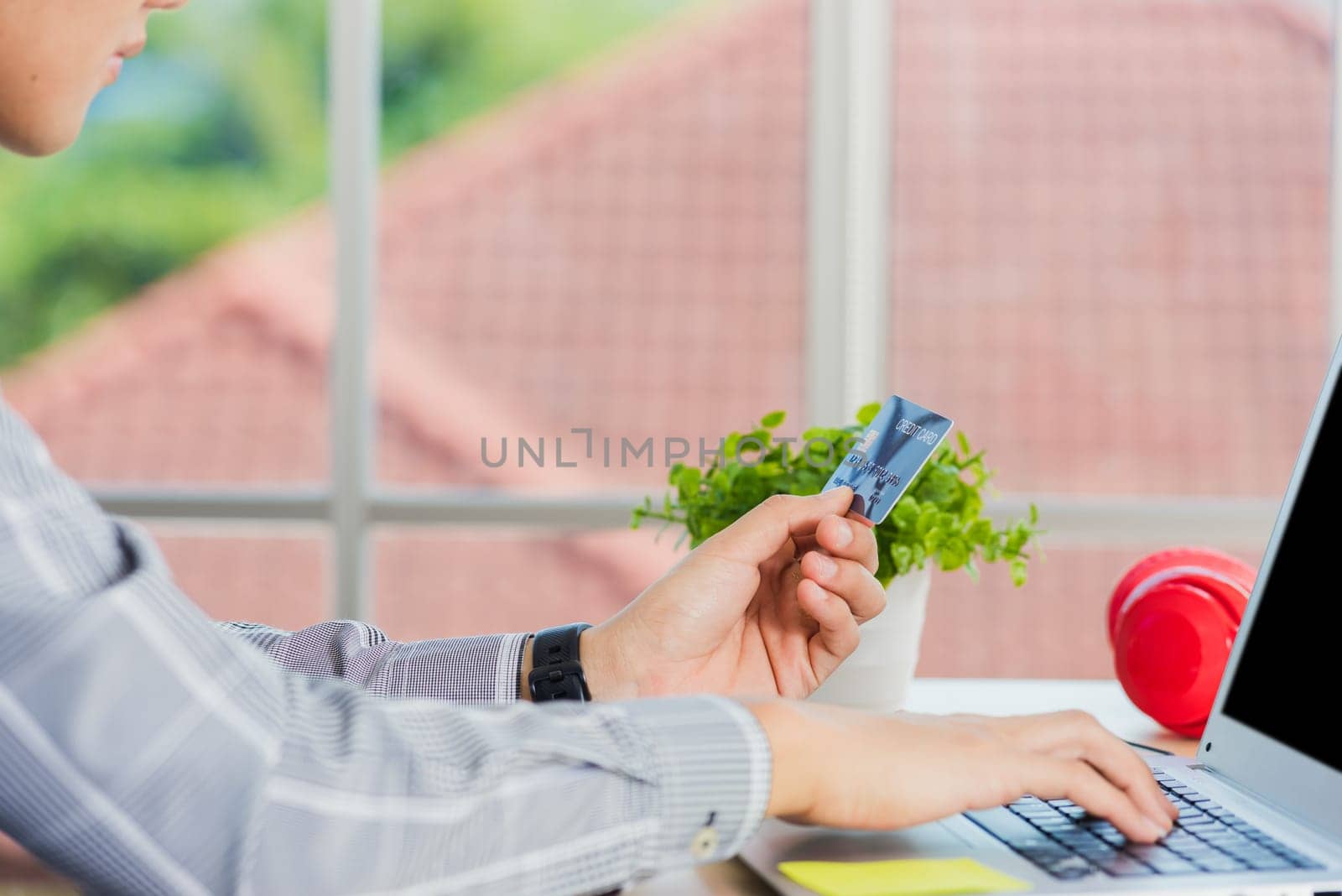 Asian business man hand holding credit card and typing entering security code on a laptop computer for process payment online shopping on the internet at the home office