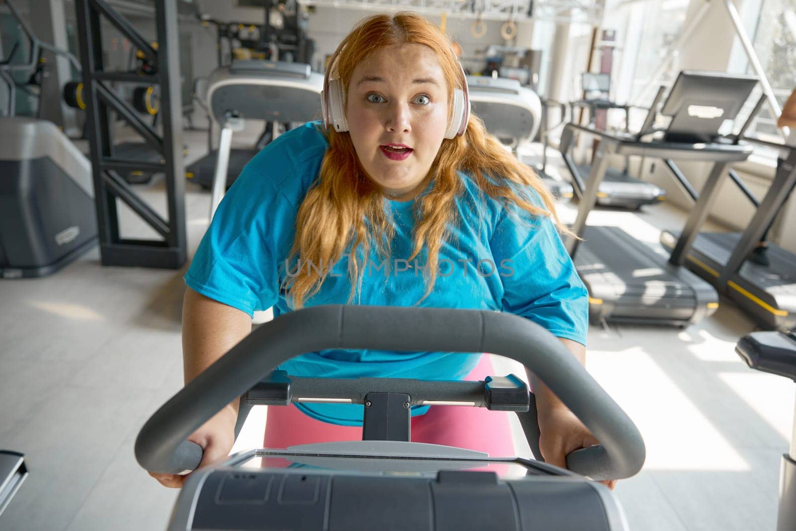 Portrait of motivated overweight woman riding exercise bike at gym. Everyday sportive routine for health and weight loss