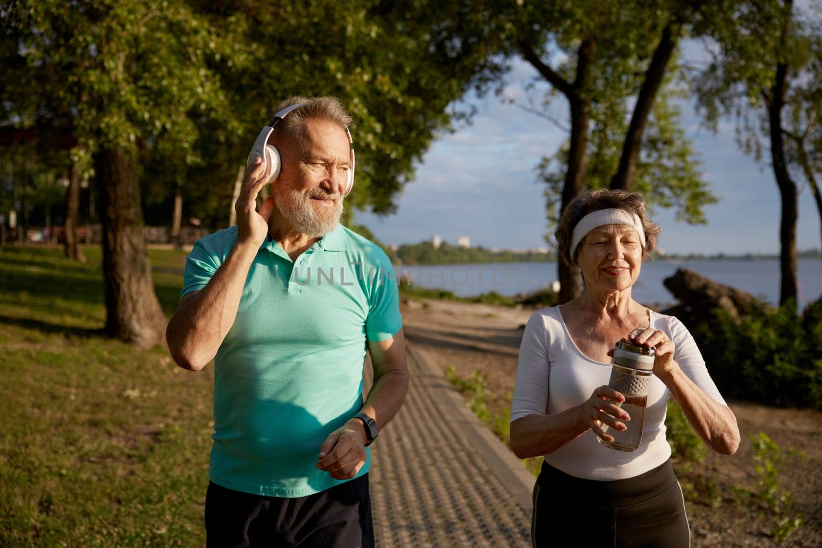 Senior man flirting with pretty elderly woman during morning jogging. Romantic date on outdoor training workout