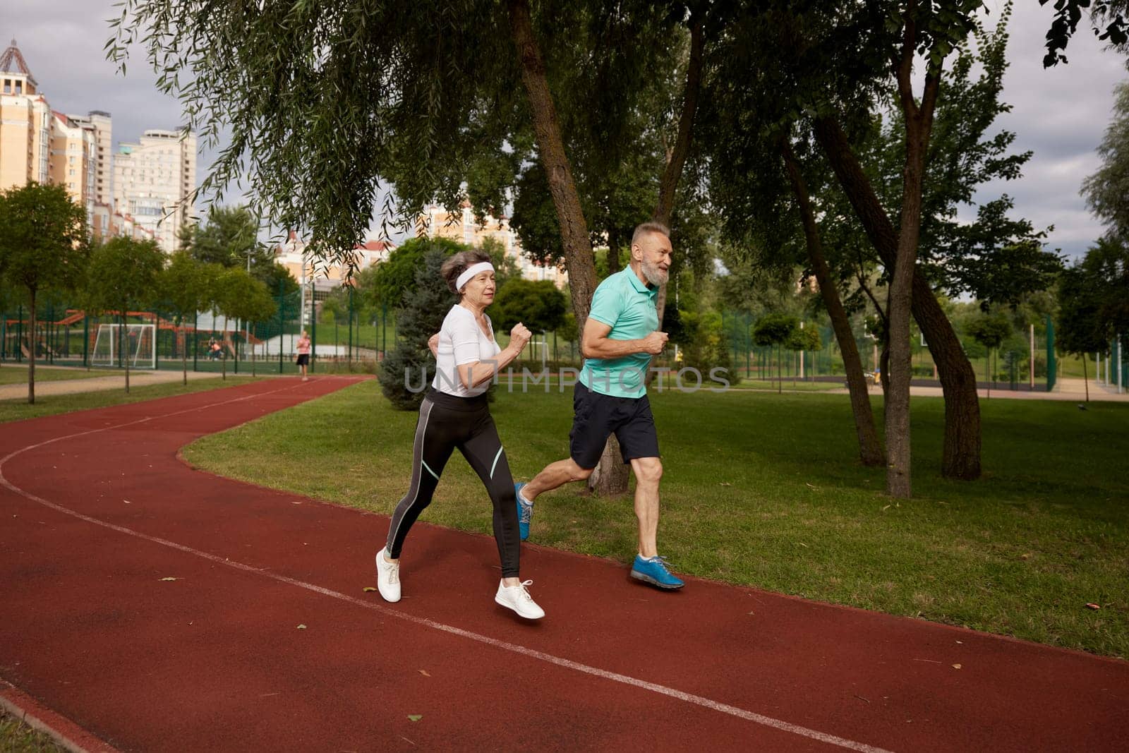 Senior couple running on track together outdoor at natural park. Happy healthy elderly woman and mature man friends exercising outdoors