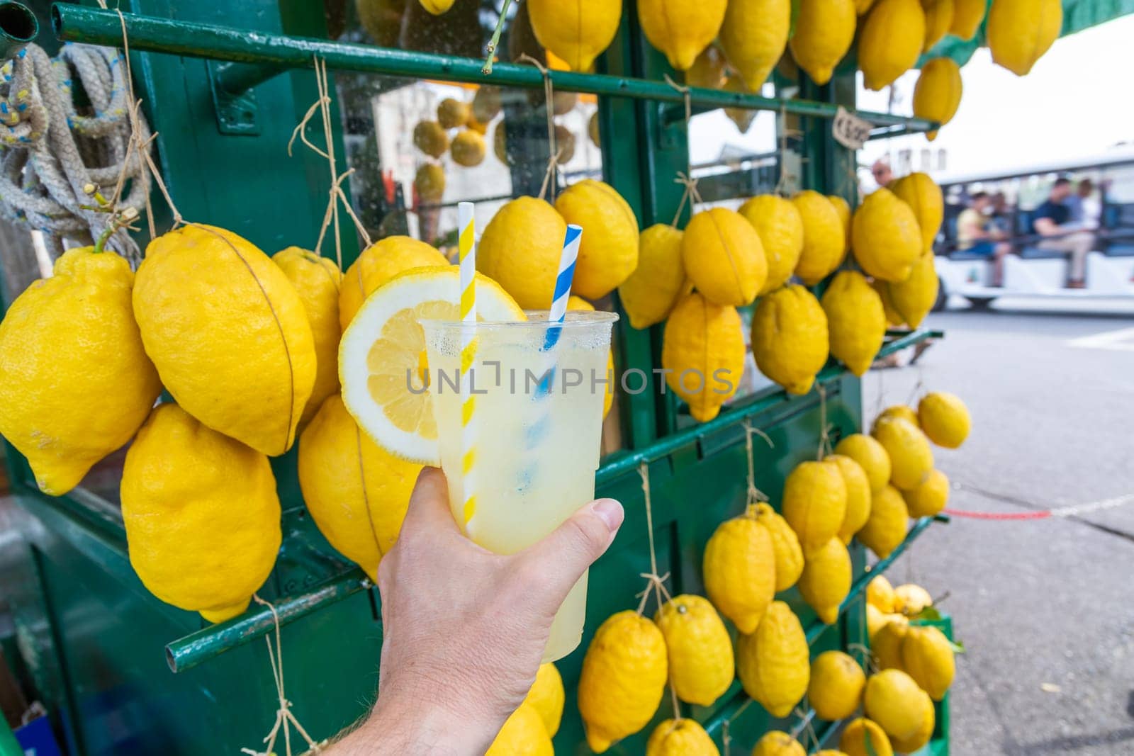 Caucasian hand with healthy fresh lemonade during summer with lemons background