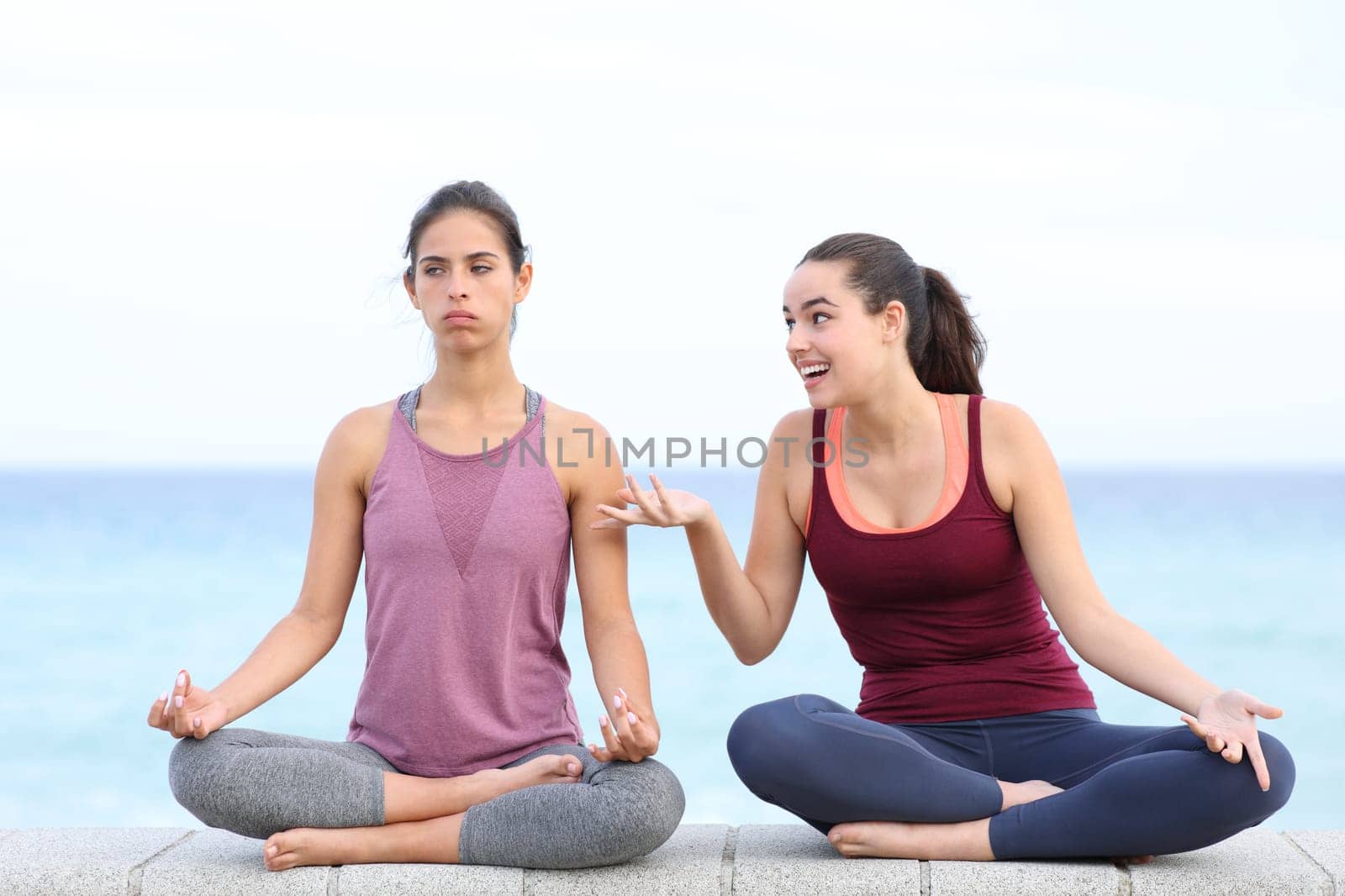 Front view portrait of annoyed yogi trying to do yoga with a friend disturbing on the beach