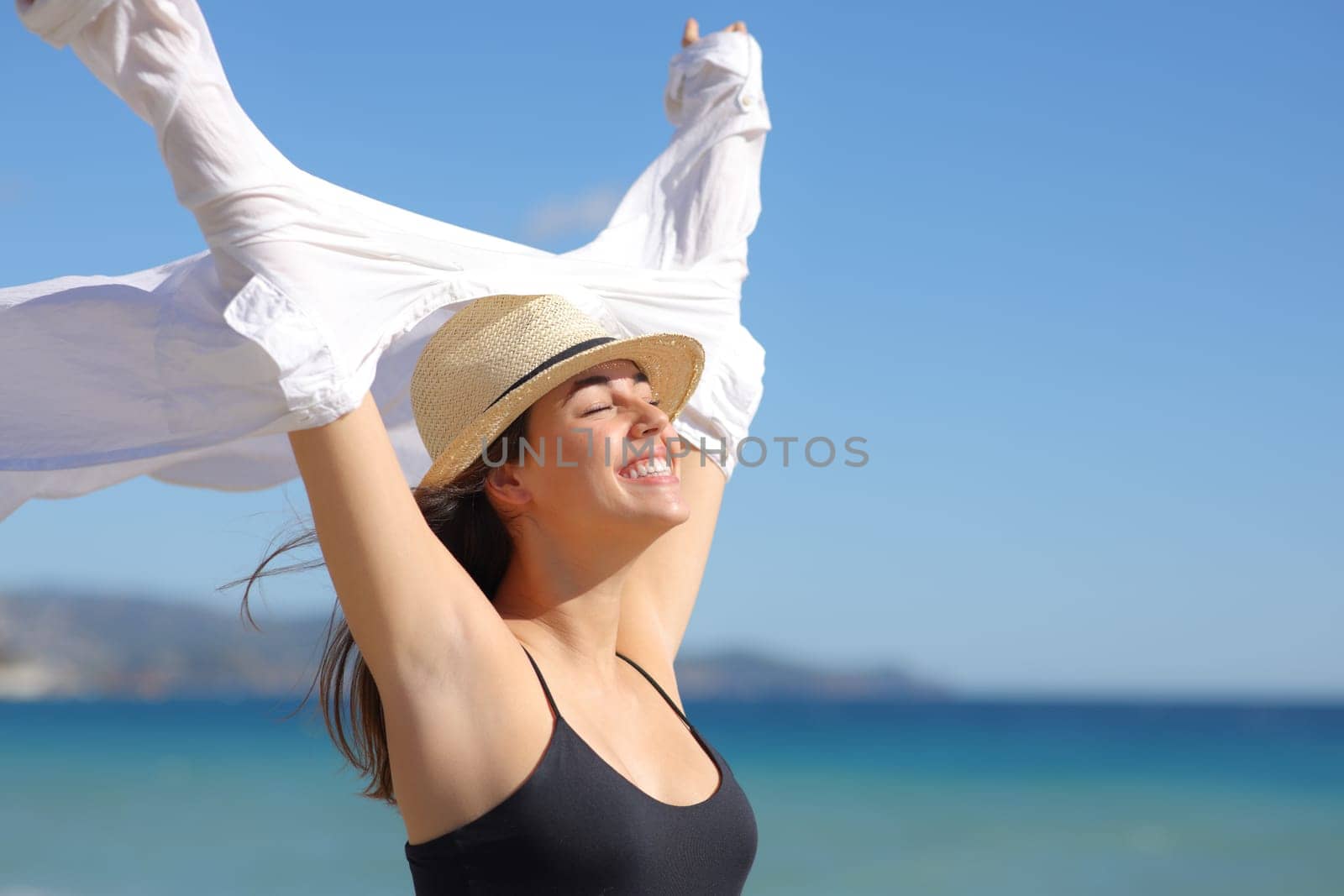Happy woman celebrating a sunny day on the beach raising arms