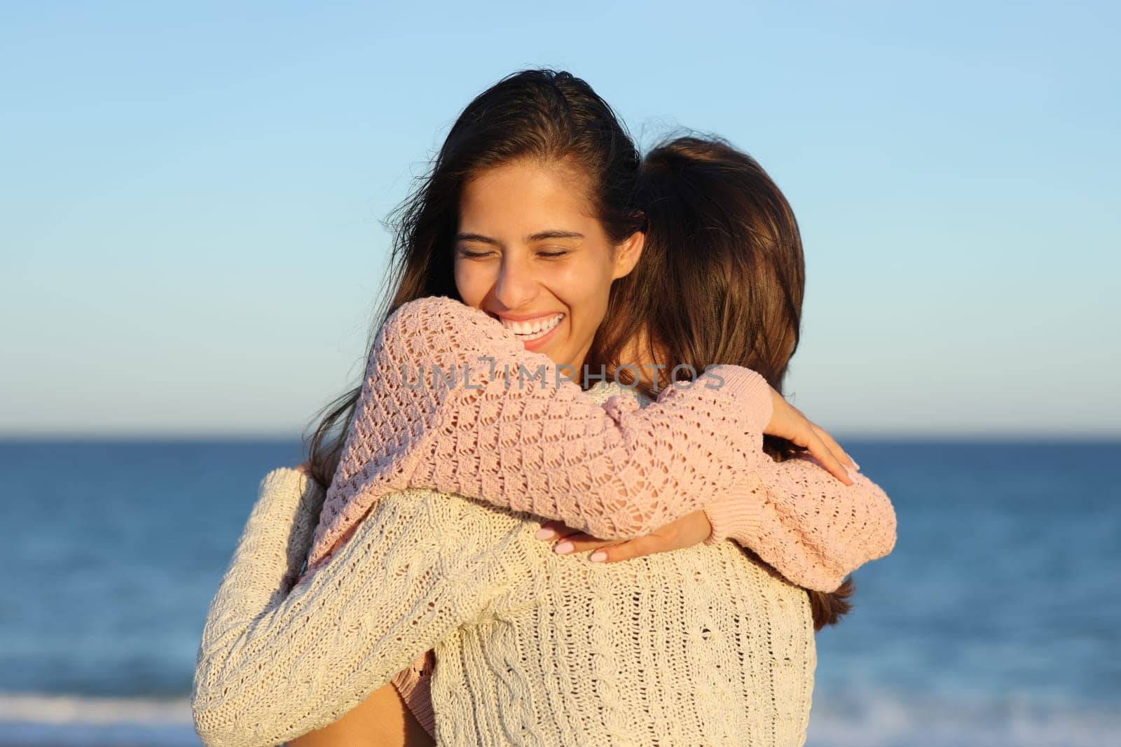 Two happy friends meeting and hugging on the beach at sunset