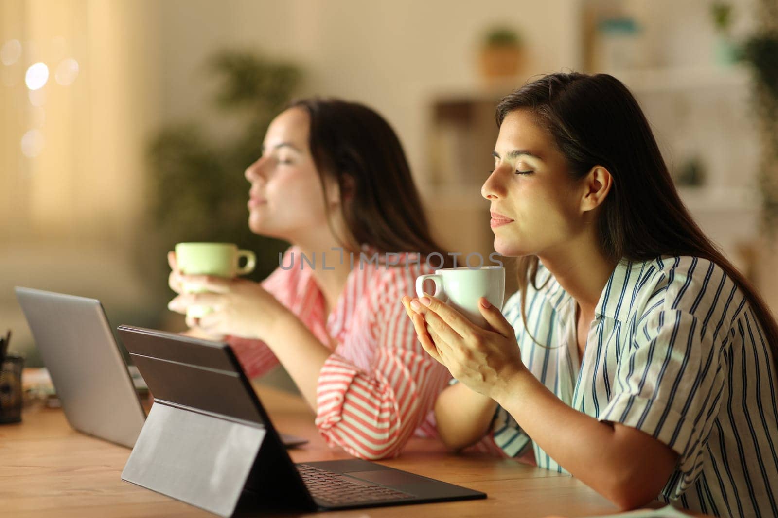 Two tele workers relaxing drinking coffee in the night at home