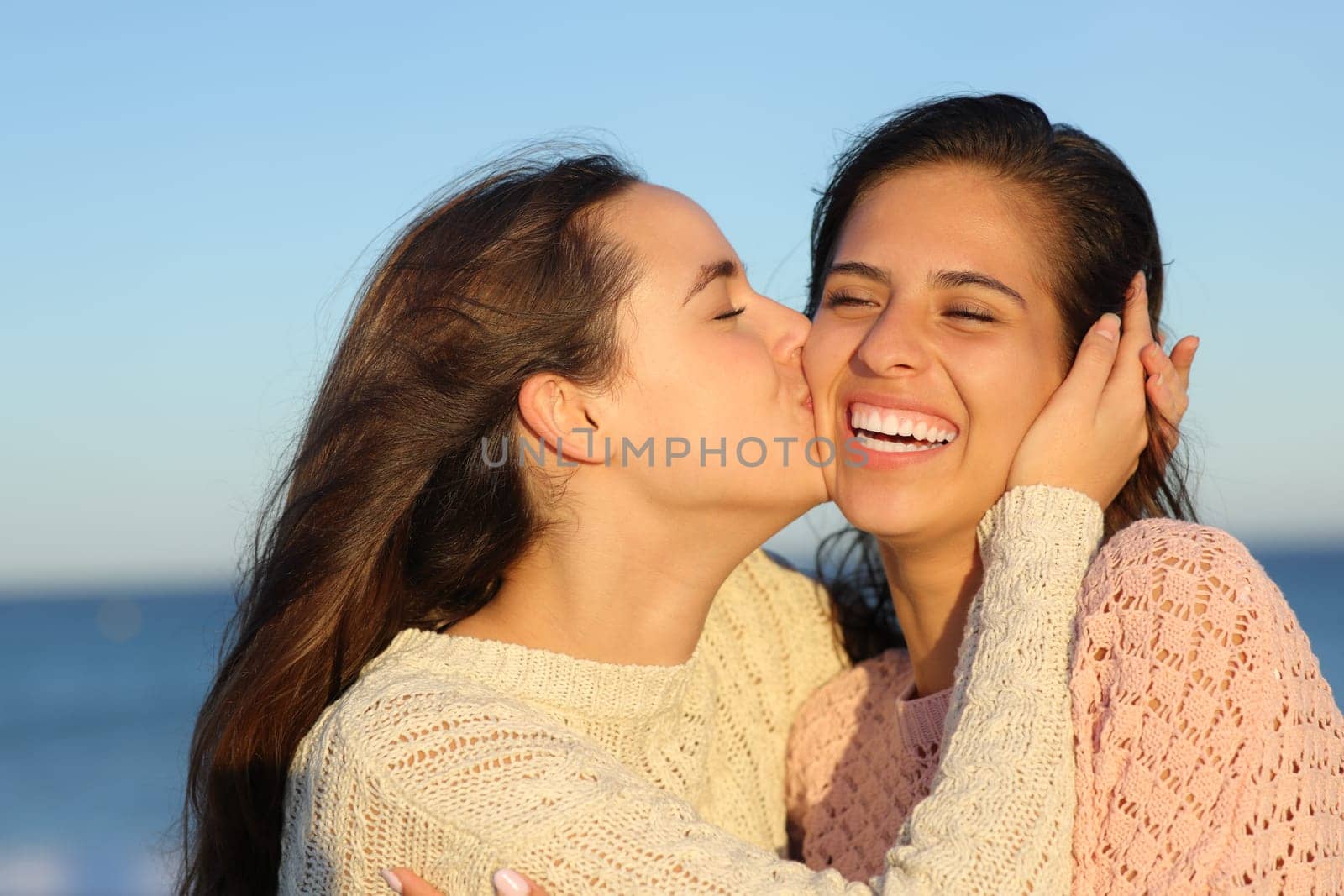 Happy affectionate woman kissing a friend on the cheek on the beach
