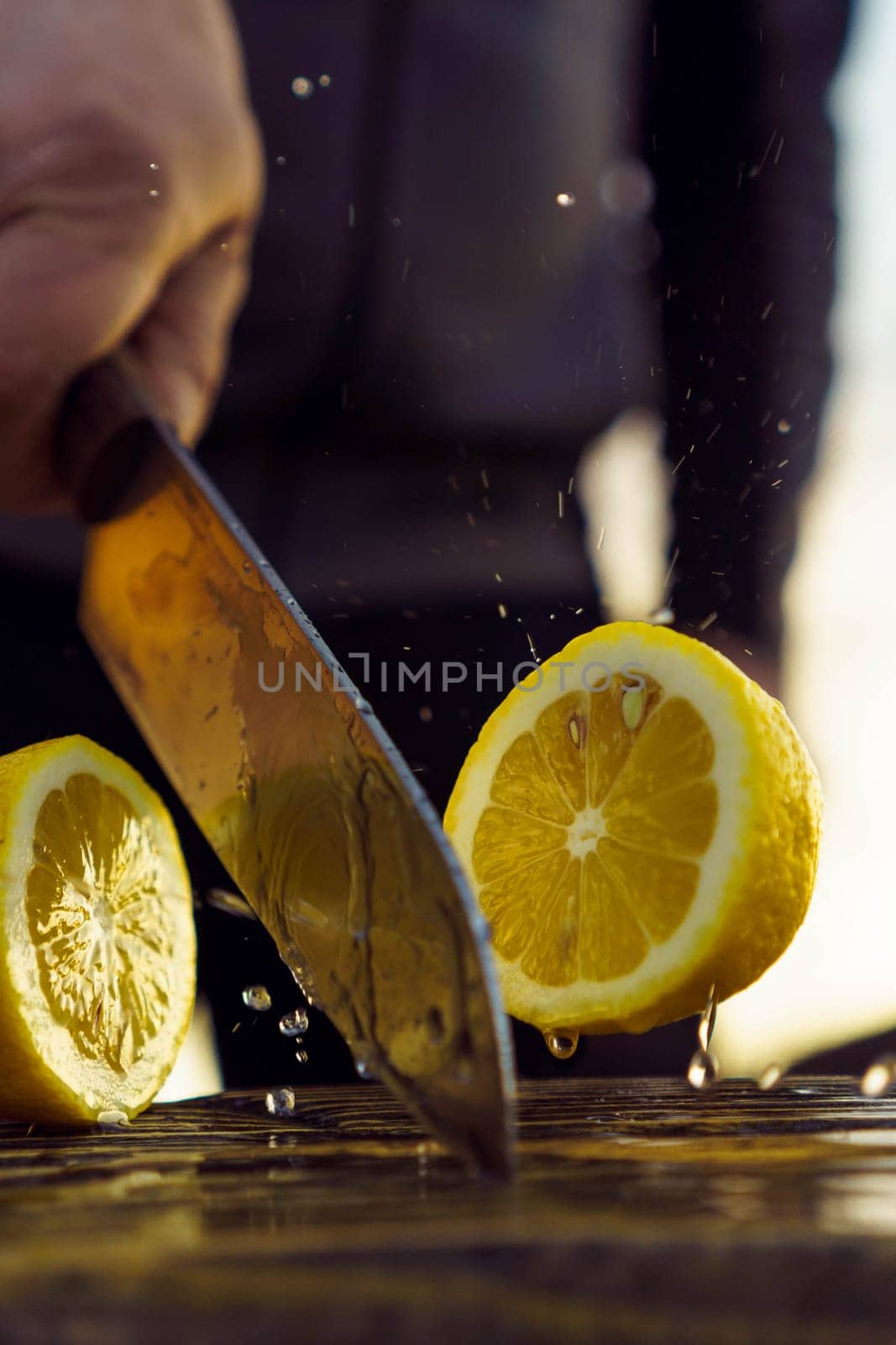 Adult man cutting lemon in half with knife. Human with knife in hand separate into two pieces juicy and sour fruit that lie on table. Yellow fruitage bounced off table and squeezed out juice.
