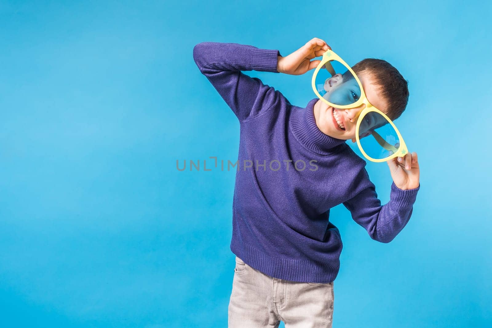 Cheerful little boy in big glasses express a surprised face isolated on blue background