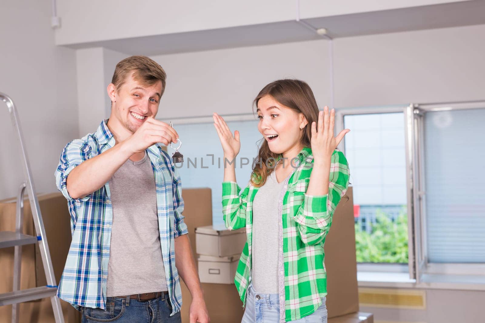 home, people, moving and real estate concept - Surprised woman looking at house keys in the hand of a man.