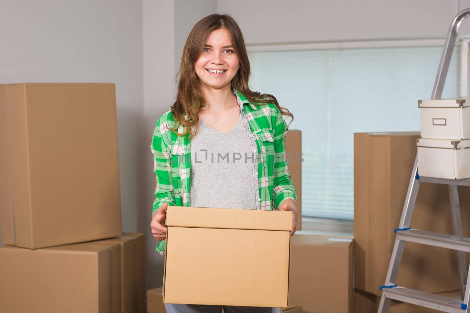Portrait of woman carrying cardboard box in new house - Moving, new home and people concept.