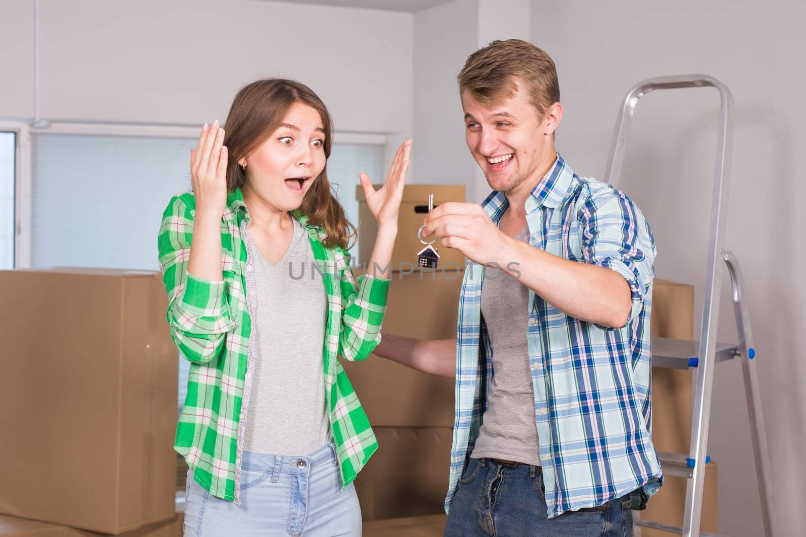 home, people, moving and real estate concept - Surprised woman looking at house keys in the hand of a man.