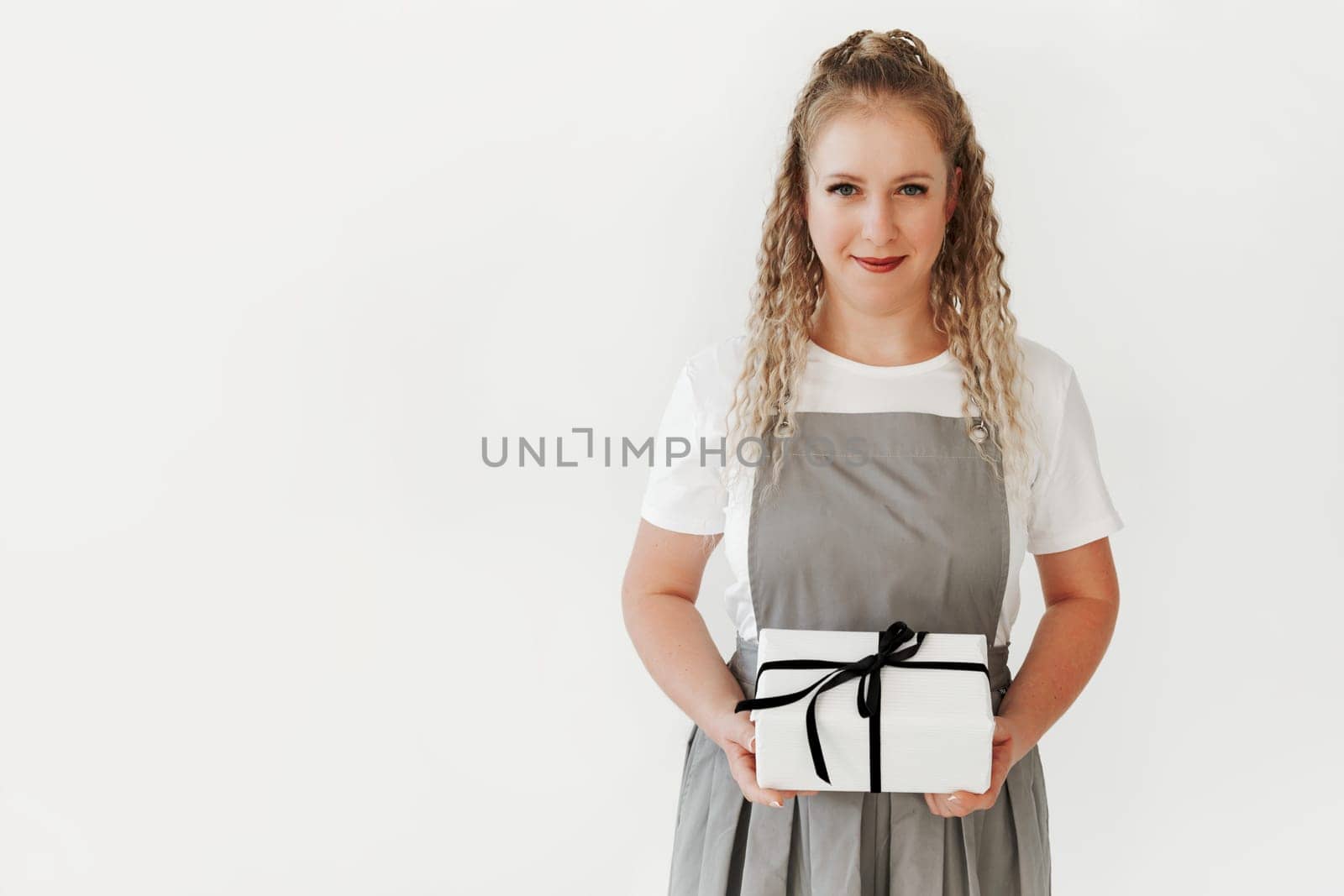 Young woman wearing apron hold in hand white present box with gift ribbon bow. Black and white. White background with copy space
