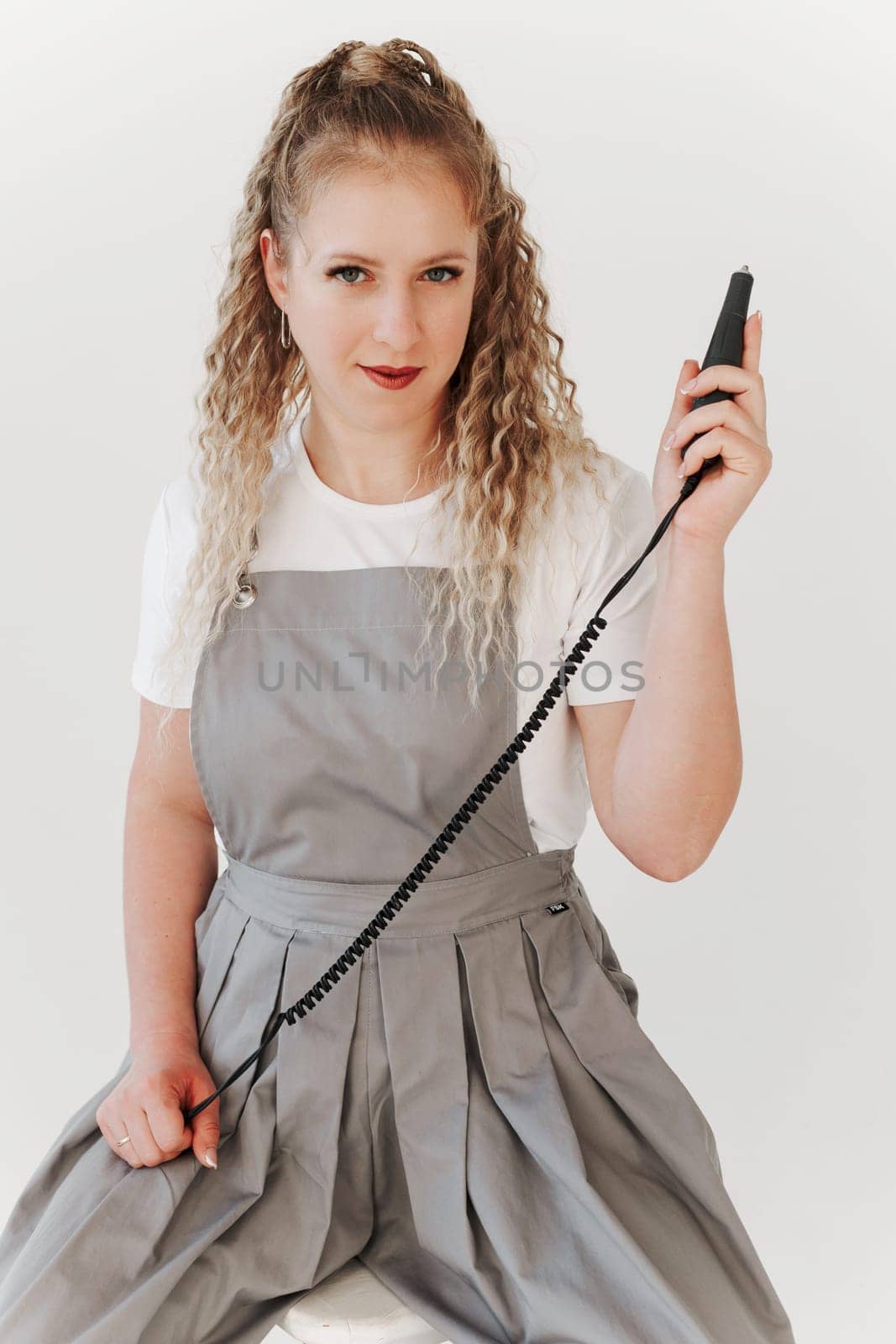Woman nails artist in gray uniform holding manicure machine in her hand. White background