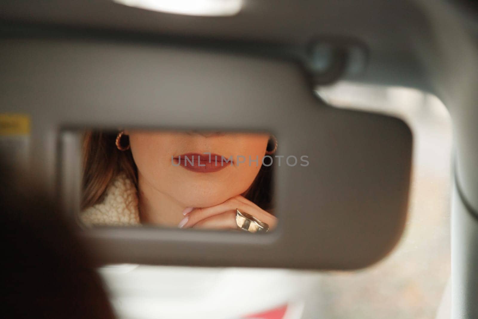 Woman lips in vanity mirror while sitting in car