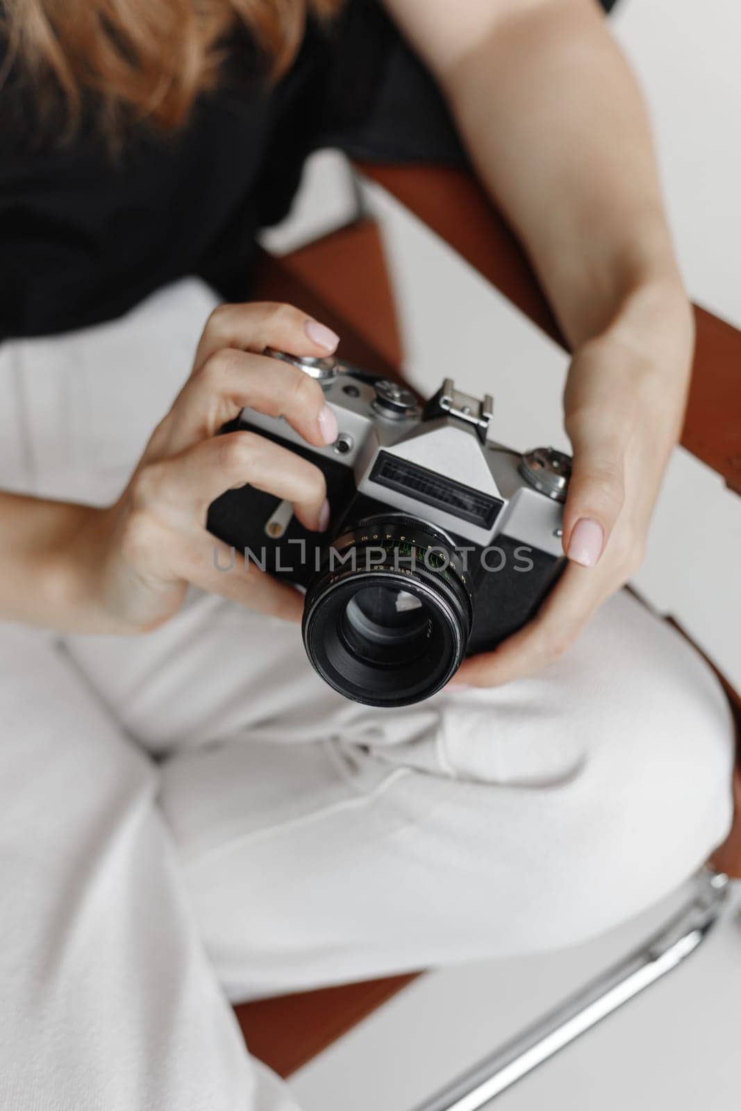 Woman holds vintage film camera sitting chair on white background.