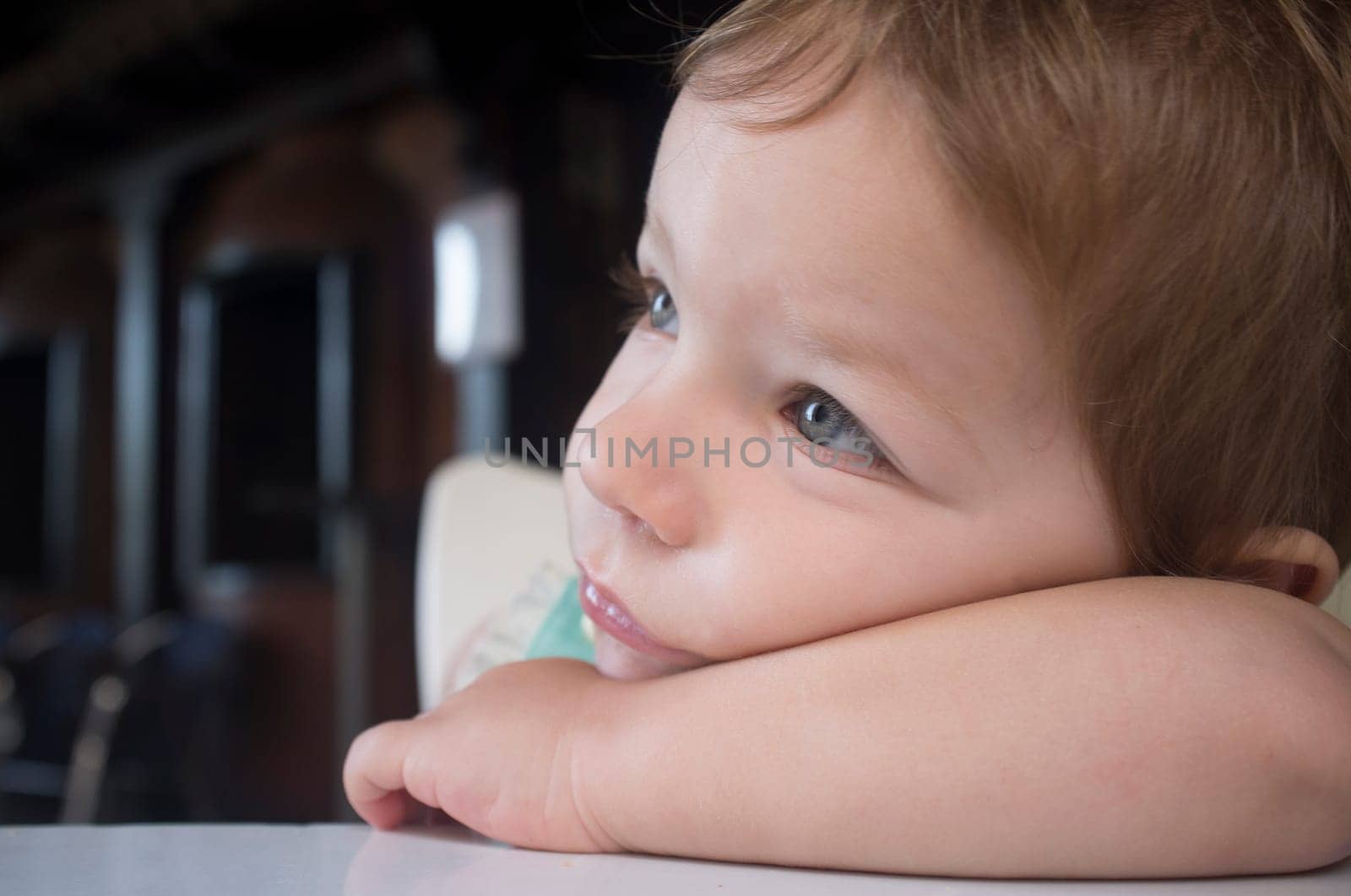 Pensive 2 years-old boy. He rests his head on his arm looking to the left