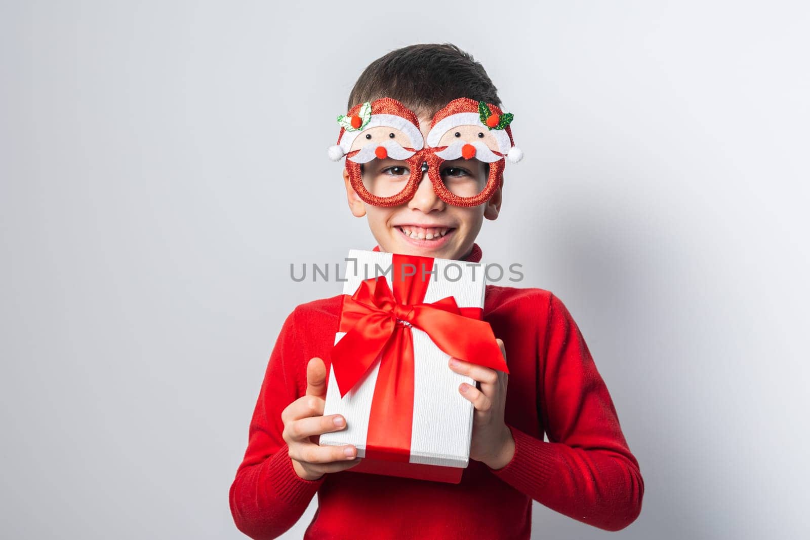 Happy boy in a red christmas holidays sweater and funny party glasses. Stylish boy with a Christmas gift have joyful on a white