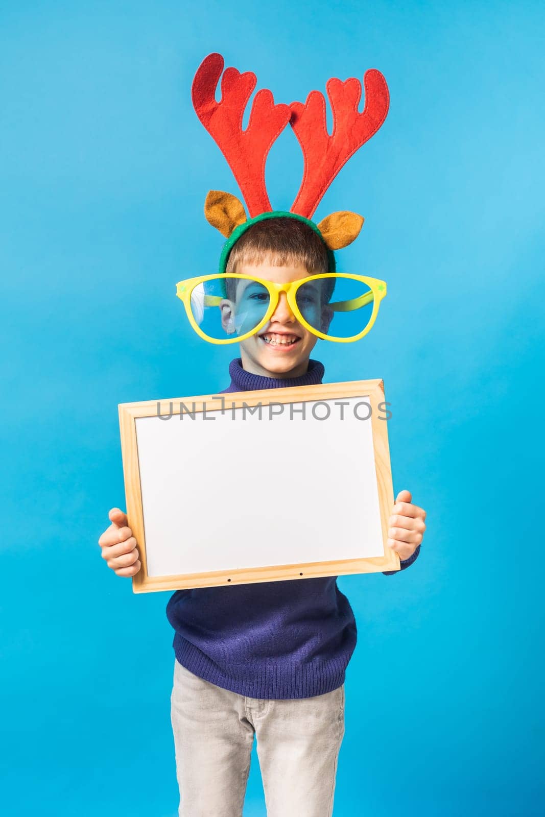Cheerful little boy generation alpha in big glasses express a surprised face holds mockup board isolated on blue background with copy space.