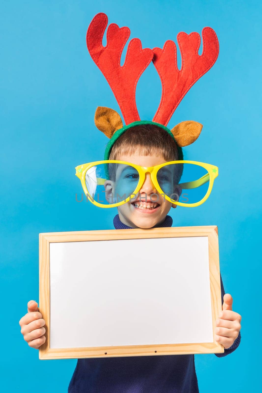 Cheerful little boy generation alpha in big glasses express a surprised face holds mockup board isolated on blue background with copy space.