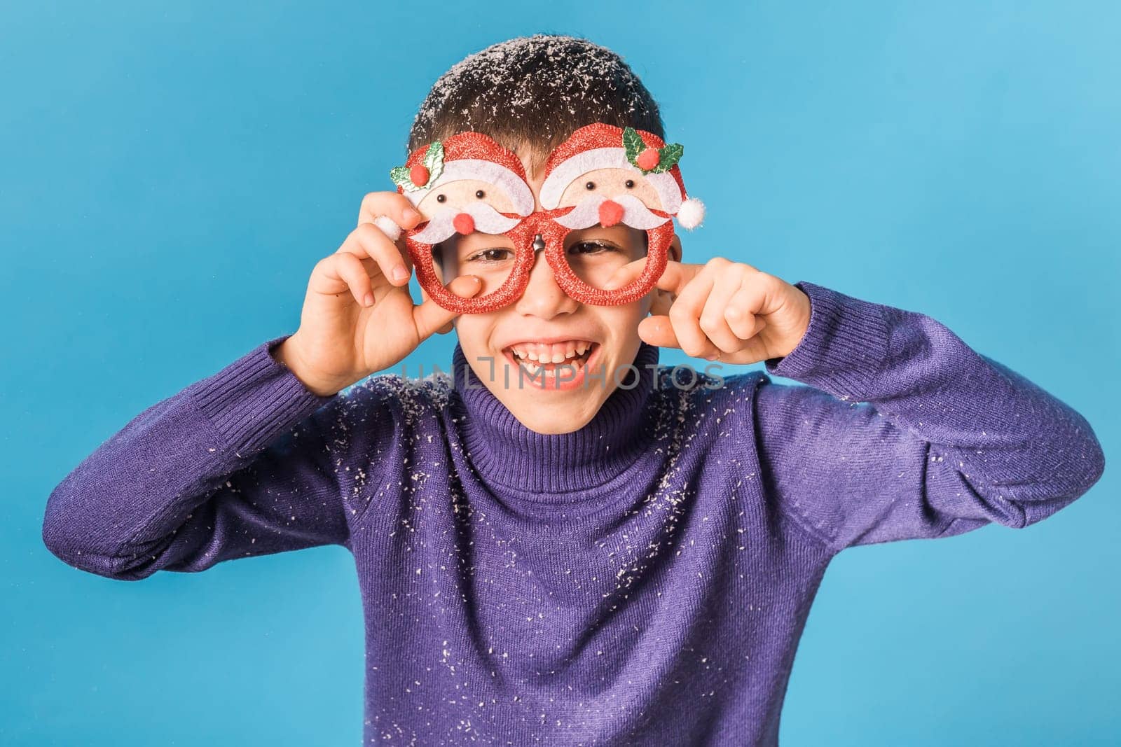 Portrait of attractive cheerful boy funny wearing festive santa eyeglasses eve christmas time isolated over bright blue color background.