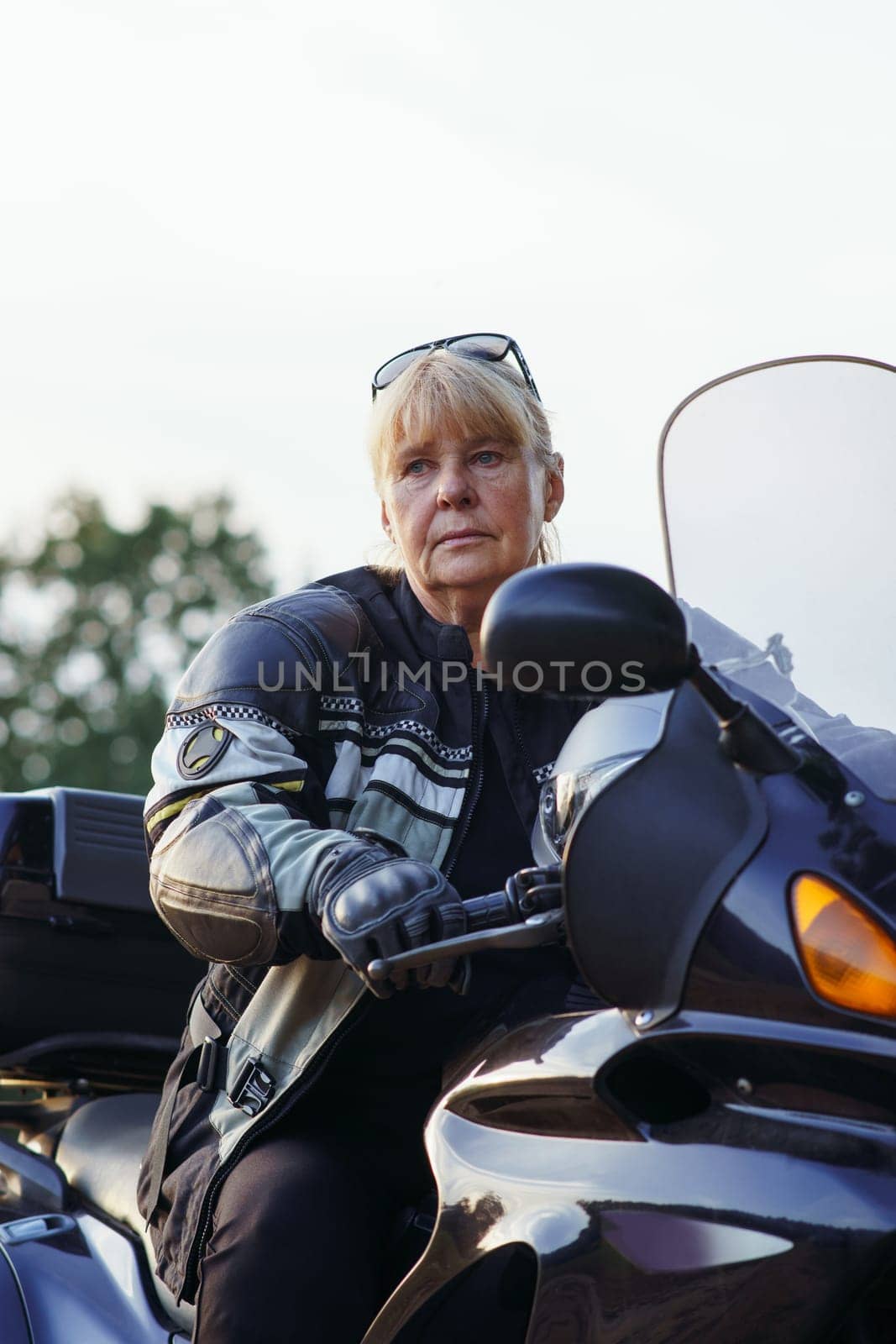 Beautiful vertical portrait of pretty middle-aged female motorcyclist sitting on her motorcycle on autumn day. Hobby motorcycle tourism. Healthy lifestyle. Excellent physical shape. Tourism travel.