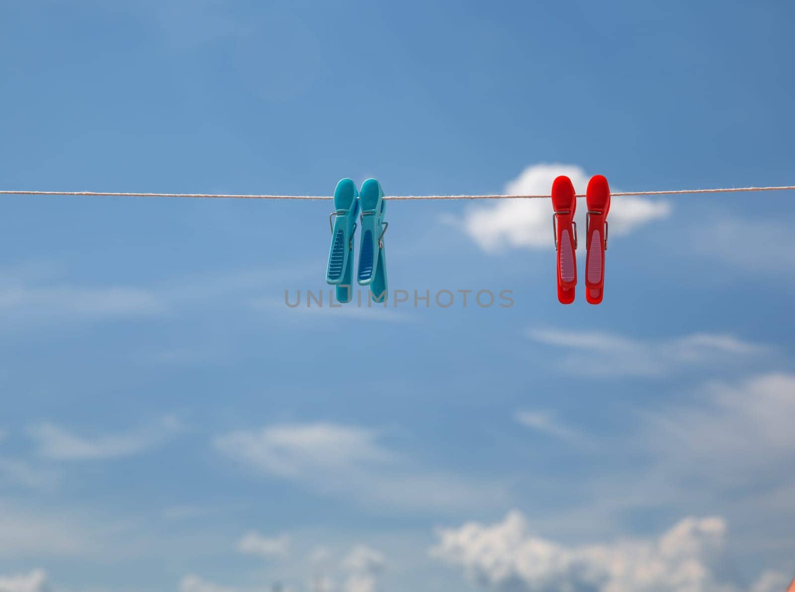 red and blue clothespins on a rope against the background of a bright blue sky with clouds. High quality photo