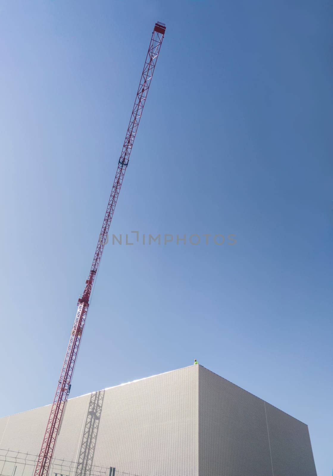 Worker on the top of a building under construction with red crane. Blue cloudy sky at background