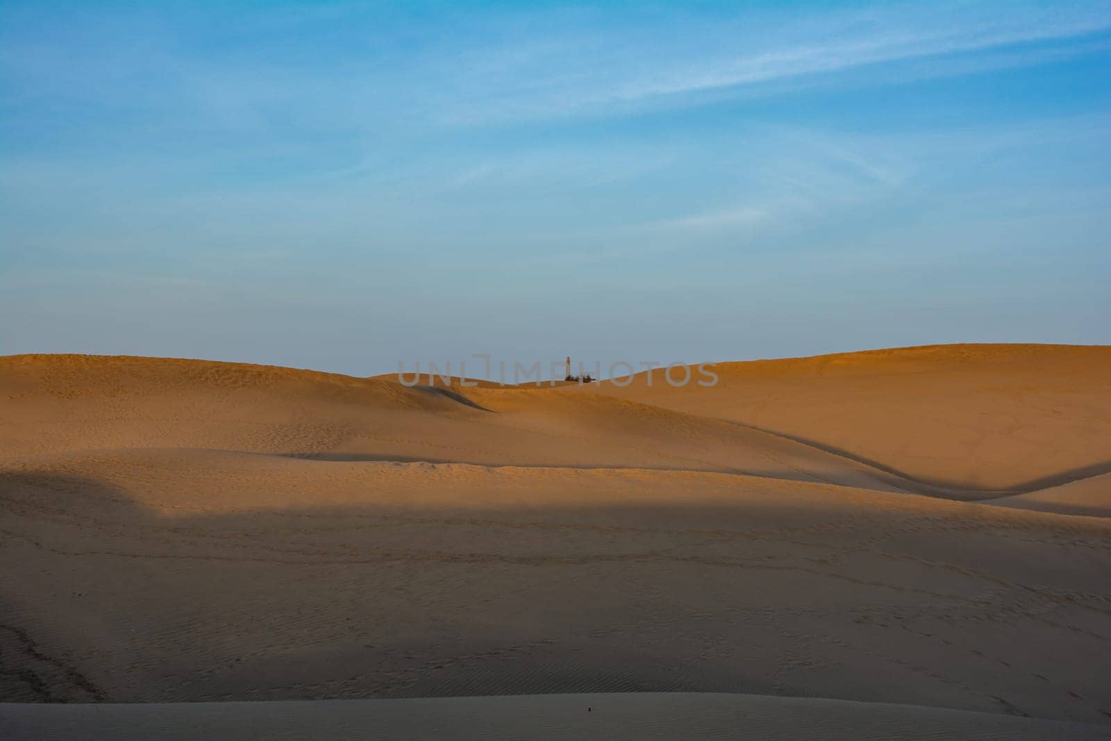 Lots of sand in the dunes of Maspalomas with the distant lighthouse on the Canary Island of Gran Canaria in Spain