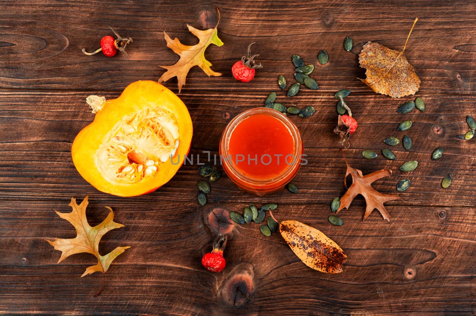 Pumpkin jam in a glass jar and fresh pumpkins on old wooden table.