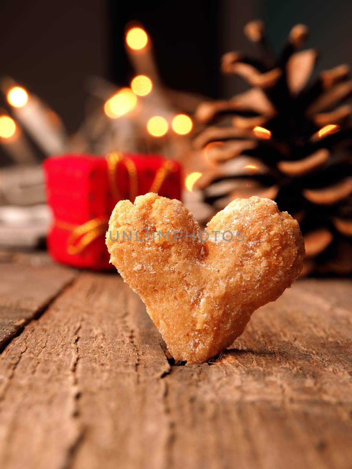 Close up of a tasty heart shaped cookie on a rustic wooden table, blurred Christmas lights and gift boxes in the background, Merry Christmas concept, giving love and peace