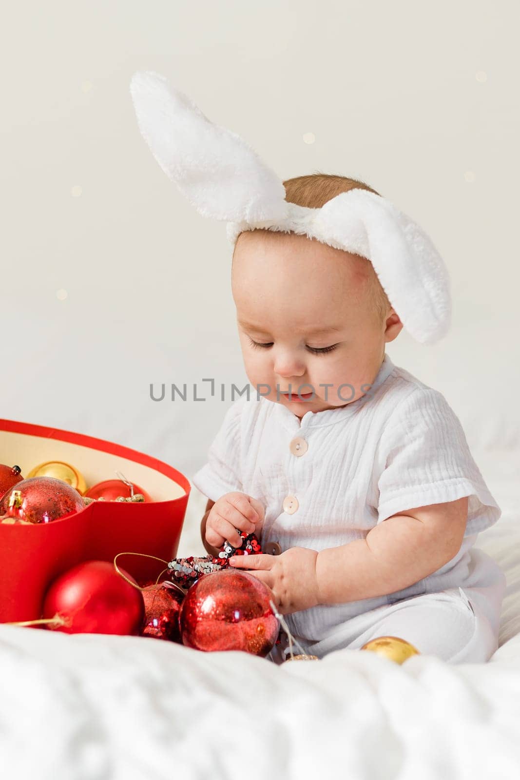Christmas Baby in Santa Hat Child playing with baubles. Present Gift Box over Holiday Lights background and Merry Christmas