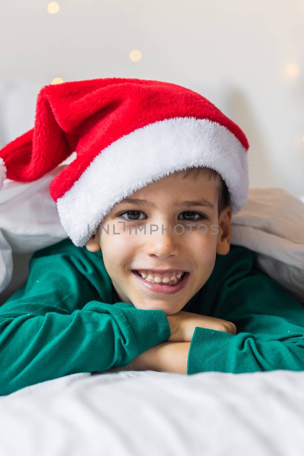 Child boy in green xmas pajamas holds a Christmas gift in his hands while sitting in bed. Generation Alpha and Gen Alpha children.