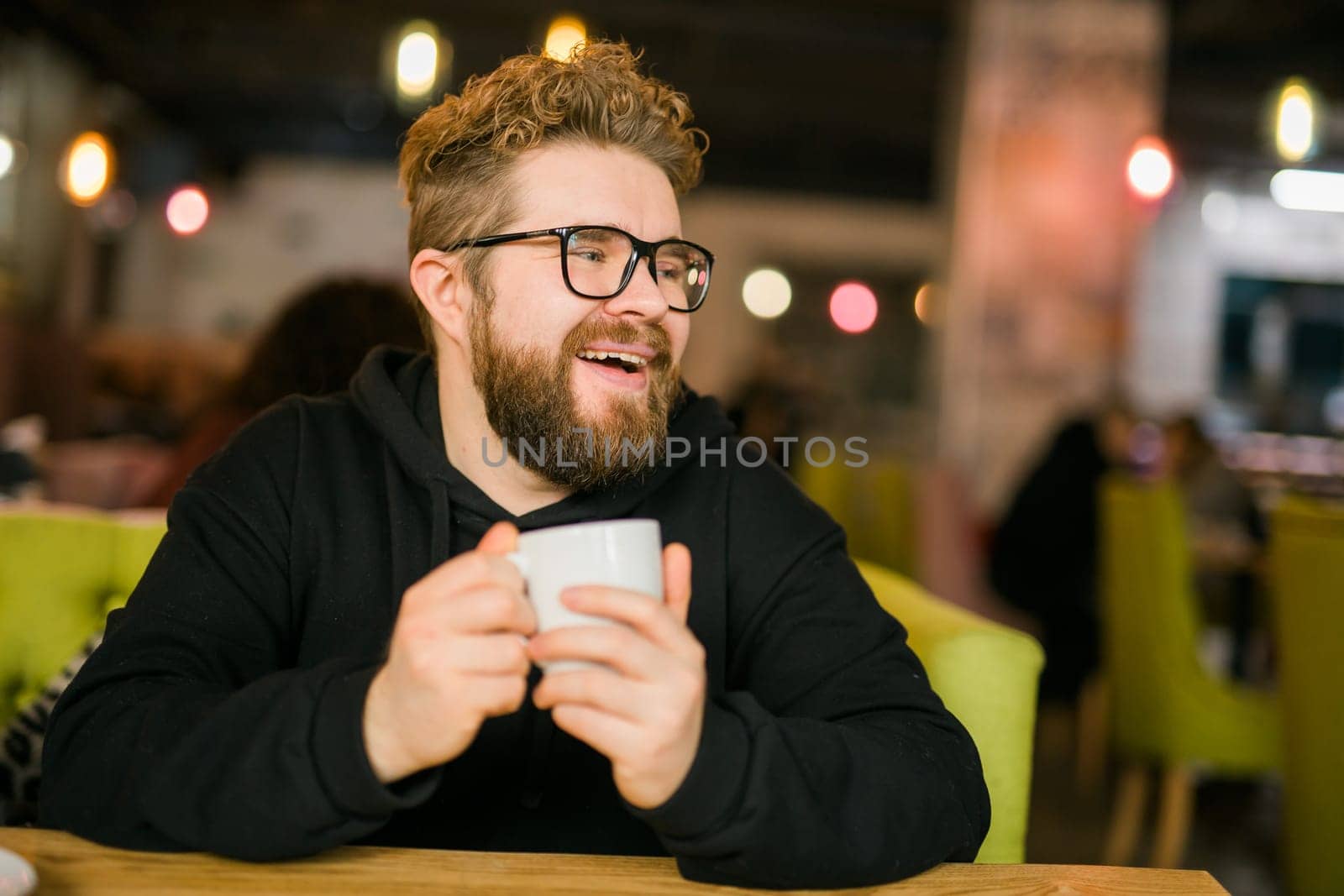 Bearded curly man smiling confident drinking coffee in restaurant or coffee shop. Millennial generation and Gen Y.
