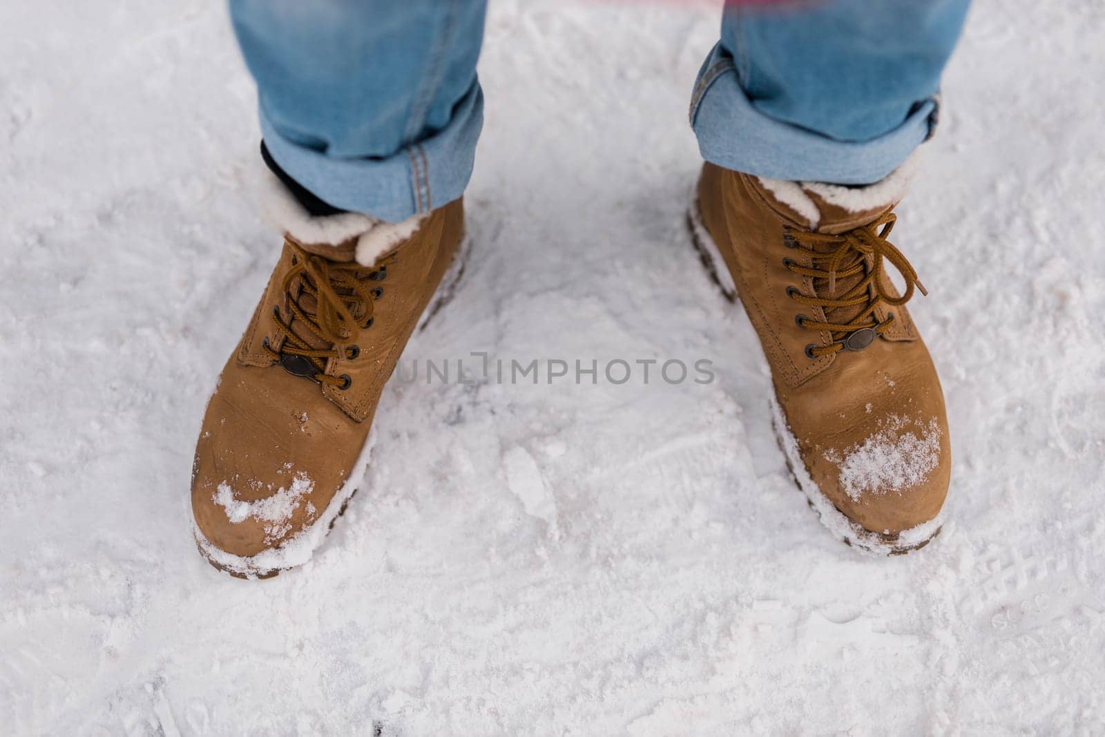 Male feet in boots walking in winter snow top view.