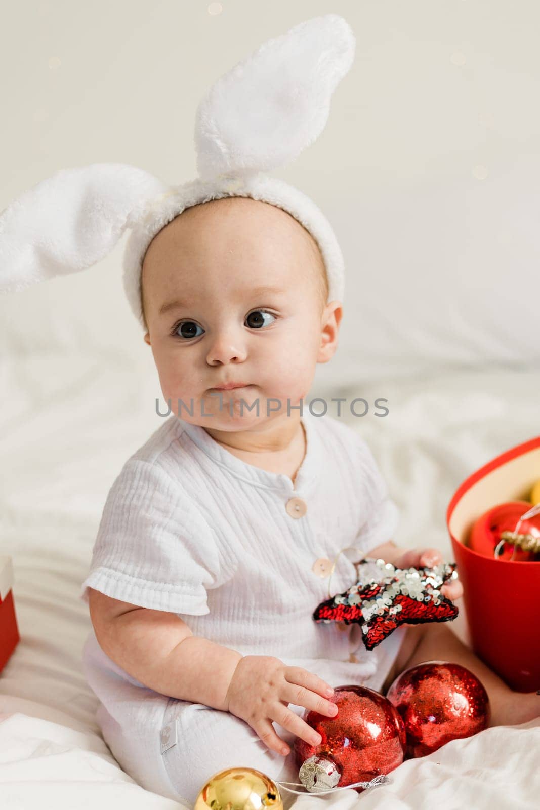 Christmas Baby in Santa Hat Child playing with baubles. Present Gift Box over Holiday Lights background and Merry Christmas