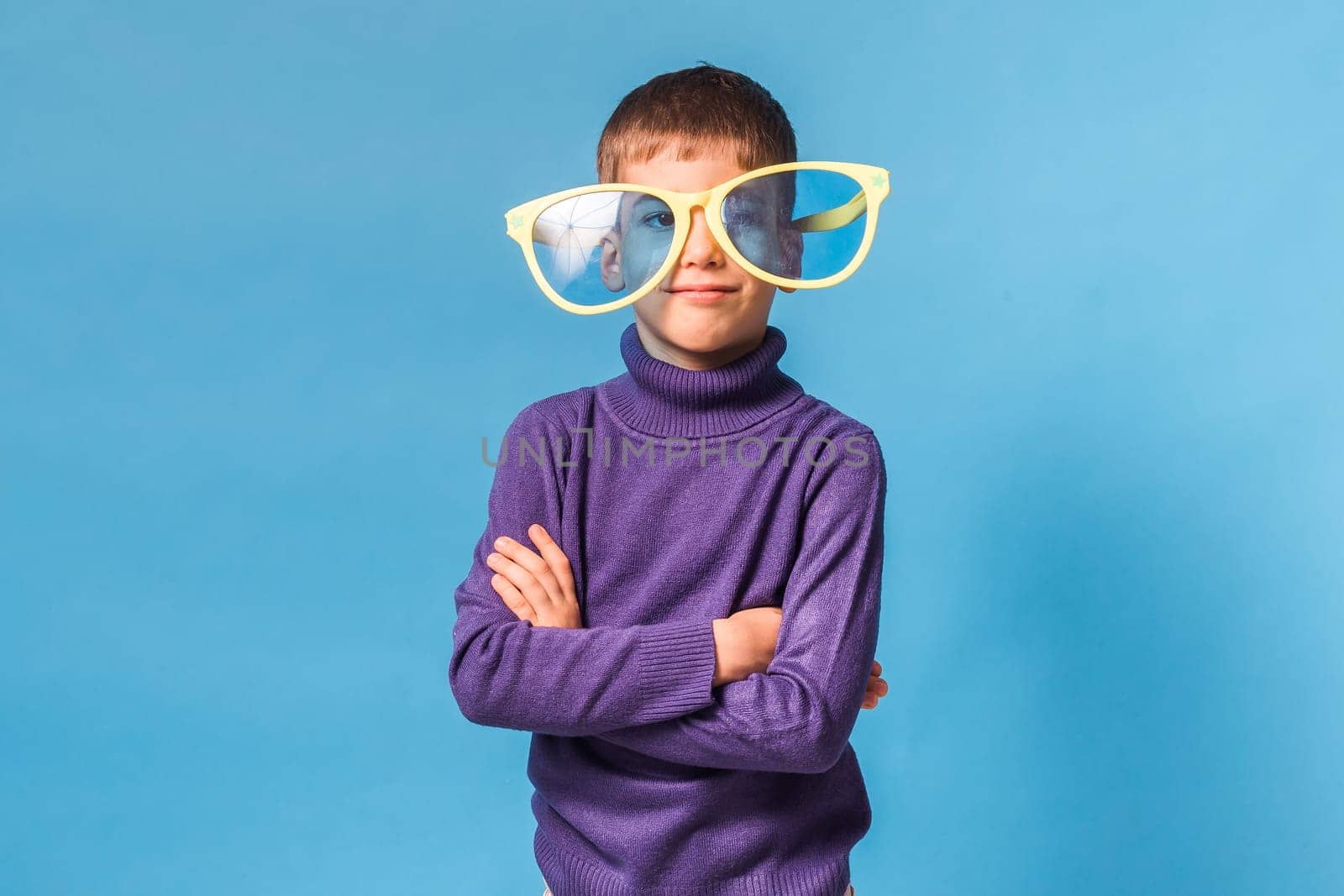 Cheerful little boy in big glasses express a surprised face isolated on blue background