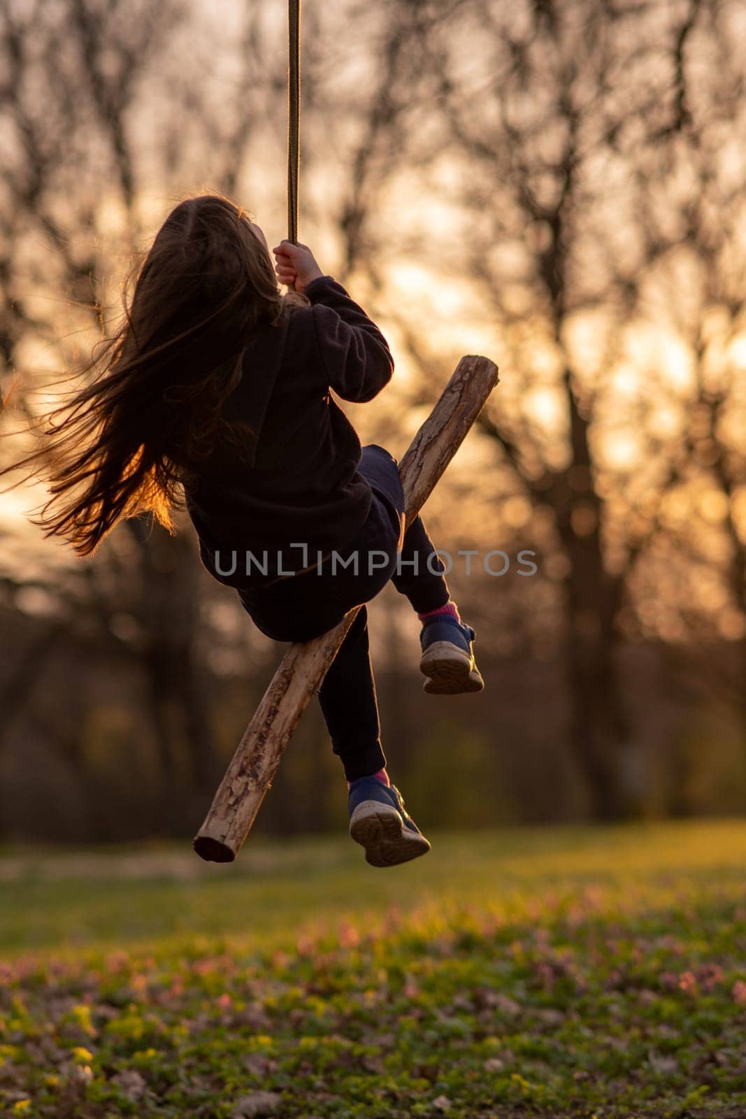 Unrecognizable little girl swings on homemade swing in nature, in park, in village, in children's camp. Outdoor games and entertainment. Happy childhood. Summer in country. Child protection.