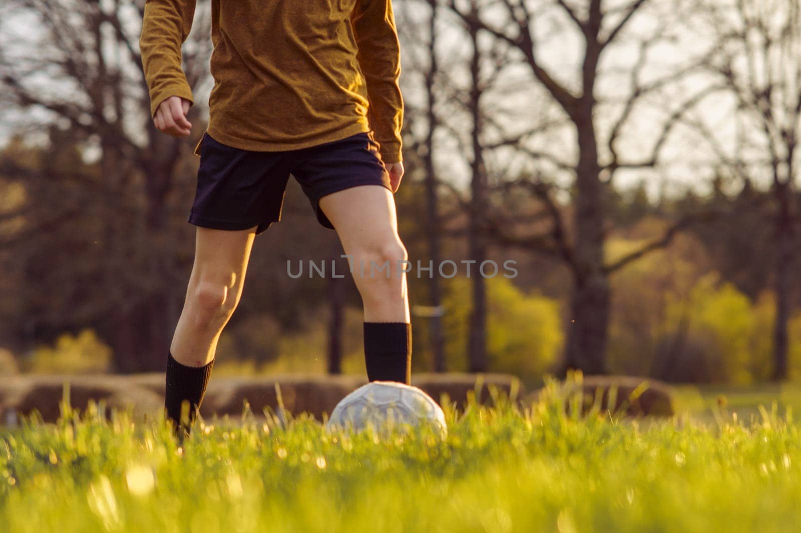 Unrecognizable teenager in sports uniform in early summer morning trains on field against background of forest . Children's sports sections. Hobbies . Football practice. Summer sports camp.