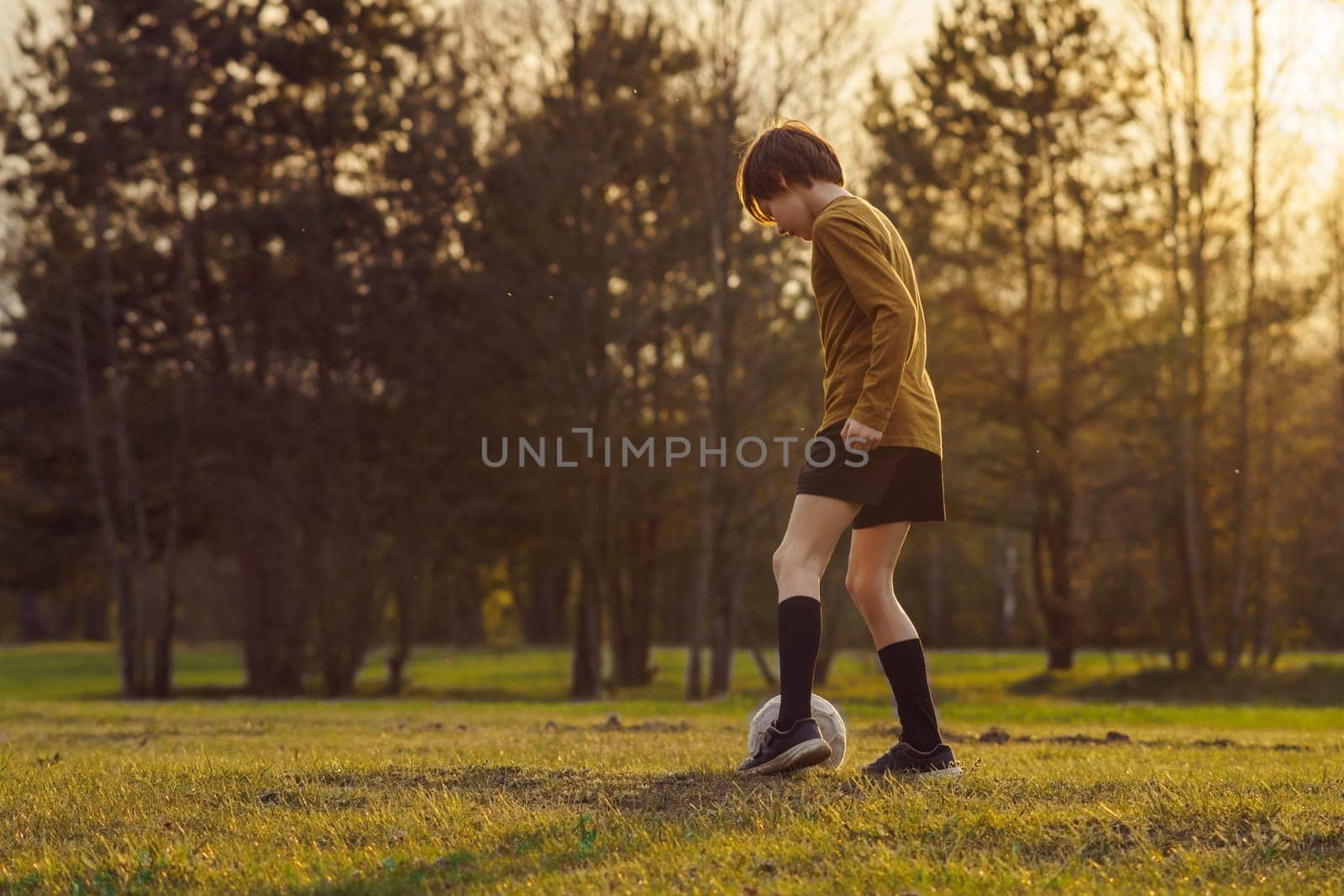 11-13 - year - old teenager in sports uniform trains on field with soccer ball in early summer morning. Sports and health. Children's sports sections. Hobbies and hobbies. Football practice.