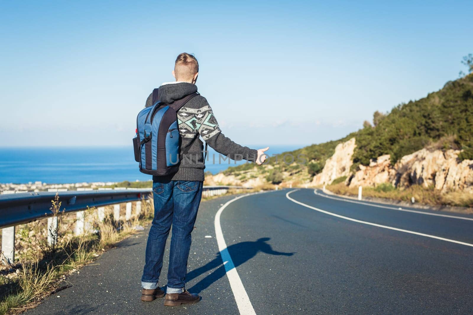 Handsome young man hitchhiker standing on a highway. Adventure and tourism concept