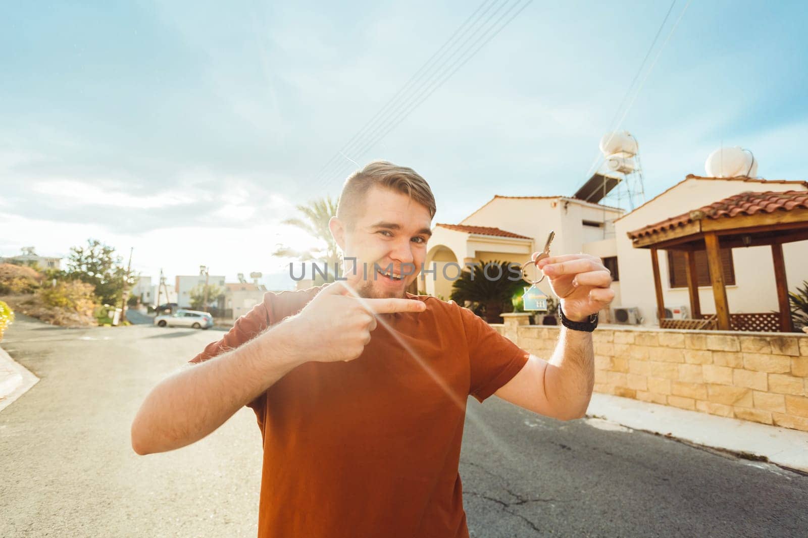 Joyful man shows keys on the background of new home.
