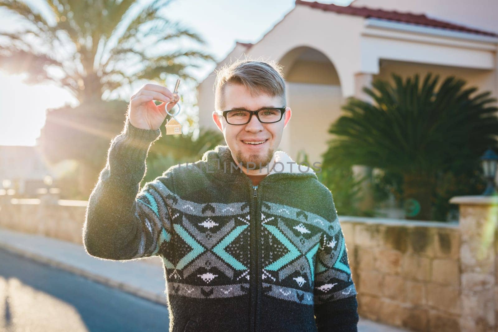 Happy funny man holds house keys on house shaped keychain in front of a new home.