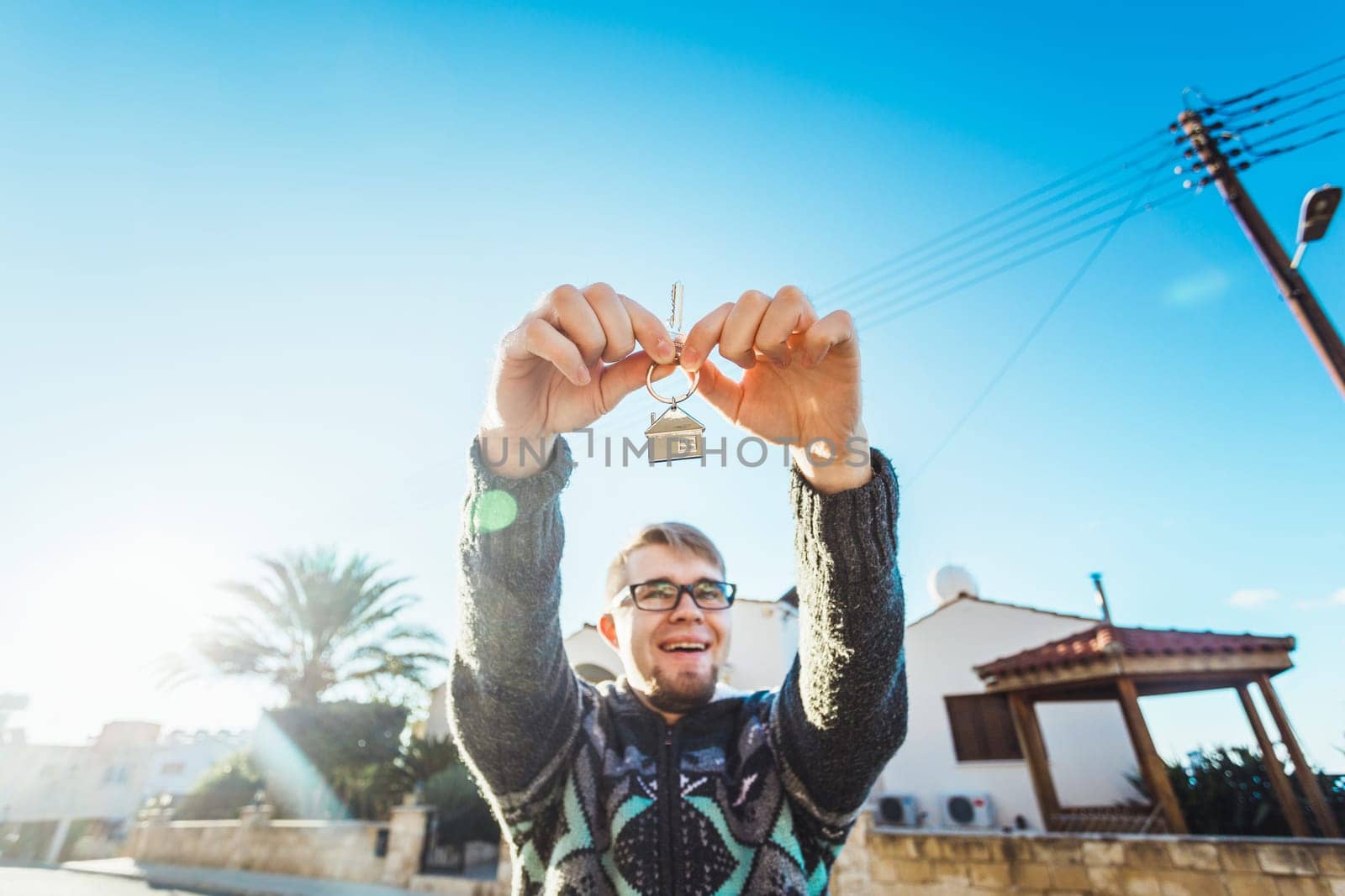 Joyful man shows keys on the background of new home.