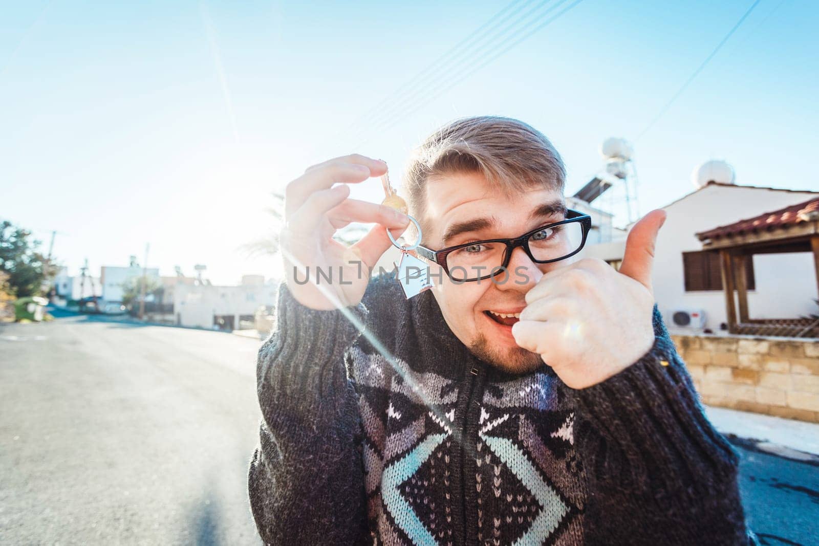 Portrait of a young man holding out new house key while gesturing thumbs up